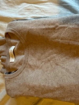 Beige cashmere-tröja från Sayless - Mjuk och stilren beige stickad tröja från Sayless i cashmere. Tröjan har rund halsringning och ribbade muddar vid halsen. Perfekt för dig som gillar klassiska och tidlösa plagg i garderoben. Storlek S