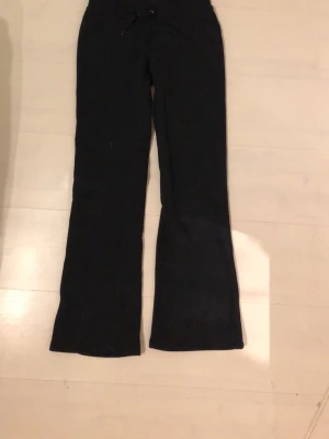 Svarta utsvängda mjukisbyxor - Säljer ett par svarta mjukisbyxor med utsvängda ben och dragsko i midjan. Byxorna har en enkel och stilren design, perfekta för en avslappnad look. Materialet är mjukt och stretchigt för extra komfort.