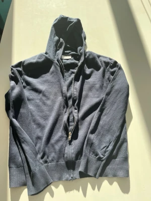Blå hoodie med dragkedja från  Grunt - En svart hoodie från Grunt med dragkedja framtill och huva. Tillverkad i mjukt bomullsmaterial och har ribbade muddar vid ärmslut och nederkant. Perfekt för en avslappnad och stilren look. Använt få gånger, pris kan diskuteras 