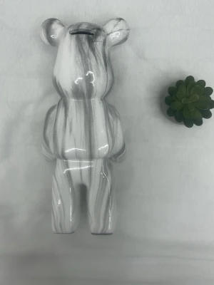 Marmorerad björnformad sp - form av en björn med marmorerat mönster i vitt och grått. Tillverkad i keramik och har ett myntinkast på toppen av huvudet. Perfekt som dekoration 