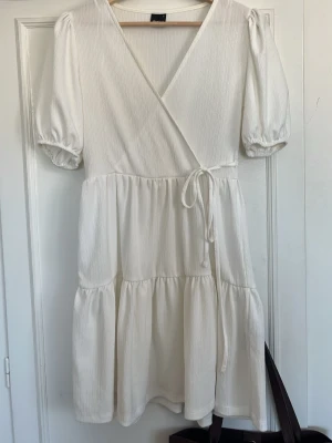 Vit omlottklänning med puffärm - Super söt vit kortklänning från Gina Tricot med omlottmodell och knyt i midjan. Klänningen har puffärmar, superfin studentklänning eller sommarklänning. Använd fåtal gånger☀️