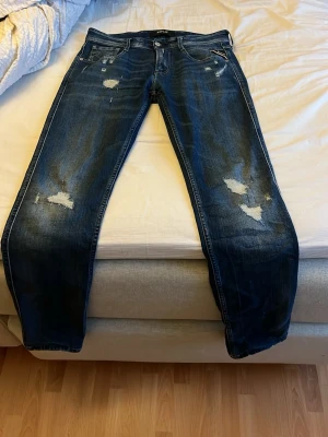 Blå slitna jeans från Replay - Säljer ett par blå jeans från Replay med slitningar och distressed detaljer på både fram- och baksida. Klassisk femficksmodell med raka ben och snygg tvätt. Perfekta för en avslappnad och trendig look. Skick:9/10 används fåtal gånger. Köpte för runt 2000kr. Mitt pris endast 699kr.