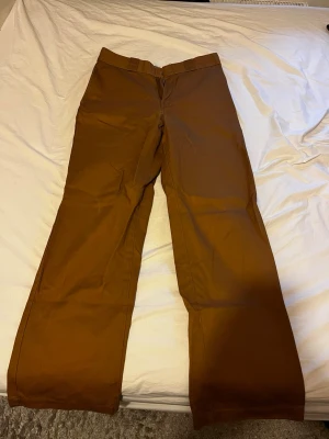 Bruna chinos från Dickies - Säljer ett par klassiska bruna chinos från Dickies med rak passform och diskreta bakfickor. Byxorna har en stilren look och är tillverkade i ett slitstarkt bomullsmaterial. Perfekta för dig som gillar streetwear och enkel stil.