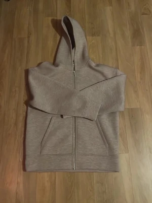 Beige hoodie  - Säljer en beige hoodie med dragkedja framtill och två stora fickor. Hoodien har en klassisk huva och ribbade muddar vid ärmar och nederkant. Perfekt för en chill och avslappnad stil. Materialet känns mjukt och bekvämt, troligen bomullsblandning.