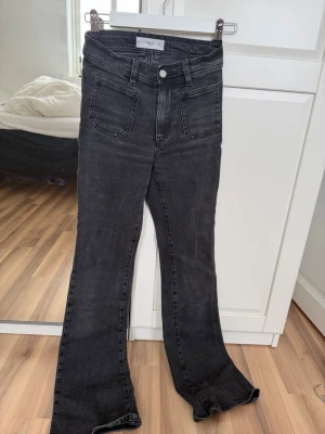 Svarta bootcut jeans från mango - Säljer ett par svarta bootcut jeans från NAKD med hög midja och stora fickor både fram och bak. Jeansen har en snygg tvättad look och är tillverkade i ett mjukt denimtyg med lite stretch. Perfekta för dig som gillar retrovibbar och vill ha ett par jeans som sticker ut.