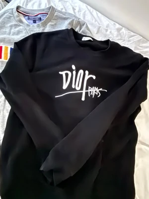 Svart sweatshirt  - Svart sweatshirt med vit grafisk logga på bröstet. Tröjan har rund halsringning och långa ärmar. Perfekt för dig som gillar streetwear och vill ha en stilren men ändå statement look.