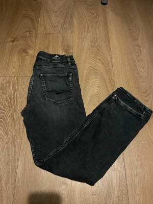 Svarta Replay jeans med raka ben - Snygga svarta jeans från Replay med raka ben och klassisk femficksdesign. Jeansen har diskreta slitningar och tydliga sömmar, vilket ger en cool och avslappnad look. Perfekta för dig som gillar stilrena och tidlösa jeans. Hör av er vid minsta lilla fråga så löser vi det