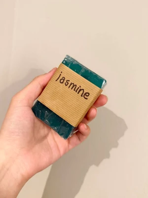 Handgjord jasmintvål havsblå - Säljer en handgjord tvål med jasmin-doft. På bandet står det 'jasmine' och baksidan har en liten dekorativ etikett. Tvålbas från Greenum. Perfekt för dig som gillar naturliga produkter.