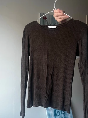 Brun ribbad långärmad topp - Mörkbrun ribbad långärmad topp med rund halsringning. Tunn och stretchig modell som sitter snyggt på kroppen. 