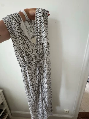 Prickig långklänning från H&M - Säljer en vit långklänning från H&M med svarta prickar. Klänningen är ärmlös, vilket ger en luftig och trendig look. 