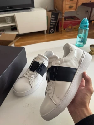 Valentino vita sneakers med svart band - Säljer nu dessa helt nya självklart äkta Valentino Opens.                                                     Dustbag Ingår, äkthetskort Ingår, låda ingår, Nordiska Kompaniet påse ingår. Pris är diskuterbart vid snabb affär, skriv till mig vid minsta frågor eller funderingar😊✅ (Kvitto finns)