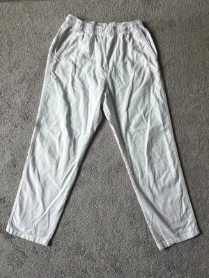 Vita linnebyxor från H&M - Säljer ett par vita linnebyxor från H&M med avslappnad passform och resår i midjan. Byxorna har raka ben och sidofickor, perfekta för en chill och luftig stil. Materialet är lätt och svalt, vilket gör dem sköna att bära under varma dagar.