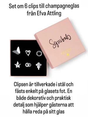 Clips till champagneglas Efva Attling - Nypris 990kr. Snyggt set med 6 olika clips till champagneglas från Efva Attling. Clipsen är i stål och har olika former som fjäril, hjärta, stjärna och ring. Perfekt för att hålla koll på sitt glas vid mingel och fest. Levereras i en rosa ask med texten 'Symbols'.