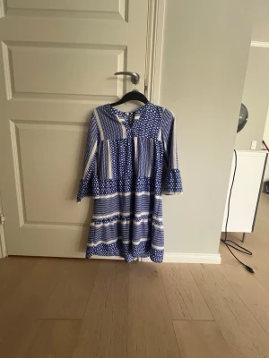 Blåvit mönstrad långklänning - Blåvit långklänning med blandat randigt och prickigt mönster. Klänningen har vidd i ärmarna, rund halsringning. Väldigt tunn och luftig. Inga täcken på slitage 