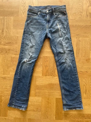 Replay jeans Thad - Säljer ett par blå jeans från Replay med snygga slitningar och distressed detaljer. Klassisk femficksmodell med raka ben och normal midja. Jeansen är i denim och har en cool, avslappnad vibe som passar perfekt till streetwear. Säljer billigt pågrund av skicket.