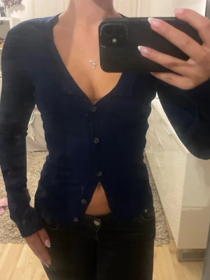 Mörkblå figurnära kofta - Snygg mörkblå kofta/ cardigan med djup v-ringning och knäppning framtill. Modellen är figurnära med långa ärmar och klassisk design, Enkel och stilren look som passar till många outfits. Tröjan är köpt i Portugal i en fin butik