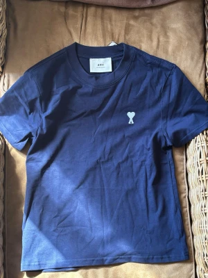 Marinblå t-shirt med A paris - Snygg marinblå t-shirt med ett A med klassisk passform och korta ärmar. T-shirten har ett vitt hjärtemblem med bokstaven A broderat på bröstet. 140, barn storlek på denna A tröjan!