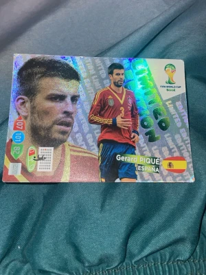 Glittrigt fotbollssamlarbild Spanien - Säljer ett glittrigt samlarkort från FIFA World Cup Brasil med motiv av en spansk fotbollsspelare i röd och blå matchtröja. Kortet har holografiska detaljer, landslagsflagga och text på framsidan. Perfekt för dig som gillar fotboll och samlarbilder.