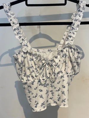 Blommigt linne - En vit topp med blå blommor från SHEIN, storlek S.