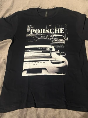 Porsche tshirt  - Cool svart t-shirt med stort tryck av en Porsche 911 GT3 på framsidan. T-shirten har klassisk passform och rund hals. Perfekt för dig som gillar bilar och vill sticka ut med en snygg grafisk design.