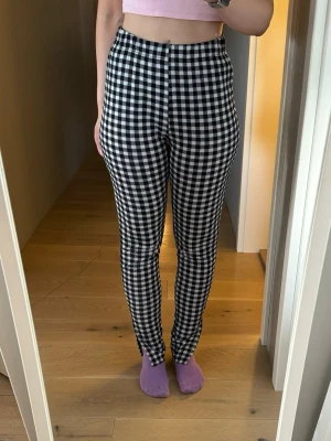 Svarta och vita rutiga leggings - Säljer ett par stretchiga leggings med svartvitt rutmönster. De har hög midja och smal passform som sitter tajt längs benen.
