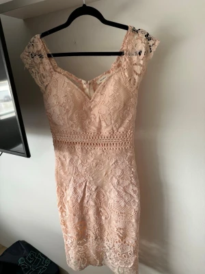 Ljusrosa spetsklänning med v-ringning - Söt ljusrosa kortklänning med v-ringning och spetsdetaljer. Klänningen har fina broderade mönster, markerad midja och korta spetsärmar. 