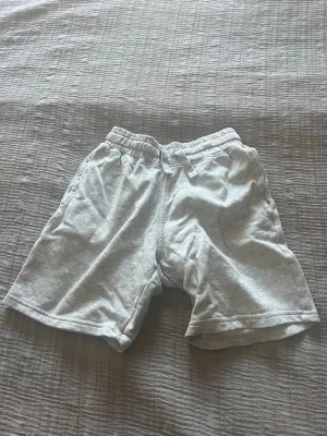 Ljusgrå bomullsshorts med resår - Säljer ett par ljusgrå shorts i mjuk bomull med elastisk midja och snörning. Shortsen har avslappnad passform och sidofickor, perfekta för chill dagar eller träning.