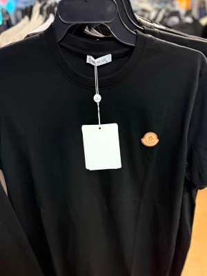 Svart t-shirt från Moncler - Snygg svart t-shirt från Moncler med klassisk rund hals och diskret logga på bröstet. Tillverkad i mjuk bomull som känns skön mot huden. Perfekt basplagg för en clean och stilren look.