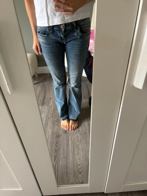 Blå bootcut jeans med låg midja - Säljer ett par klassiska blå bootcut jeans med låg midja och fem fickor. Jeansen har en snygg tvätt och raka ben som går ut lite nedtill. Perfekta till sneakers eller boots och passar till många olika stilar.