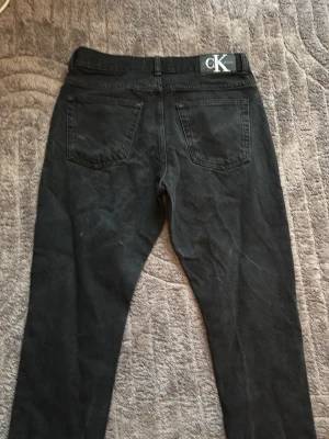 Svarta skinny jeans från Calvin Klein - Säljer ett par svarta skinny jeans från Calvin Klein med klassisk femficksdesign och logga på linningen bak. Jeansen har smal passform och är tillverkade i stretchigt denimtyg för en bekväm känsla. Perfekta för dig som gillar en clean och stilren look.