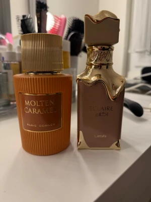 Molten Caramel & Eclaire parfymduo - Två exklusiva parfymer: Molten Caramel från Paris Corner i en rund, räfflad orange flaska med gulddetaljer och Eclaire från Lattafa i en elegant beige och guld flaska med unik form. Båda flaskorna har lyxiga detaljer och sticker ut på parfymhyllan. Båda är full size men lattafa eclaire har cirka 70% kvar och spray locket saknas.