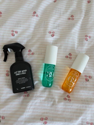 Parfymset med spray från Lush & Sol de Janeiro - Säljer ett parfymset med tre olika body sprays. En svart sprayflaska från Lush 'Let The Good Times Roll' och två färgglada flaskor från Sol de Janeiro, en grön (No. 39) och en orange (No. 62). Alla flaskor har modern design och tydliga etiketter.