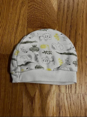 Vit barn / baby mössa med sött djurmotiv - Fin vit babymössa med ett gulligt djurmönster i grönt och gult! Motivet består av elefanter, lejon, fåglar, krokodiler och grodor – en charmig mössa som passar både till vardag och utflykter! Storlek: Storlek saknas på etiketten, men jag uppskattar att den passar barn som är ca 0–2 månader. Säljs i bra skick! Kika gärna in på mina andra annonser, jag säljer just nu flera baby- och barnkläder! Hör av dig vid intresse eller frågor!