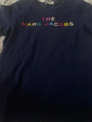 Blå Marc Jacobs t-shirt med tryck - Snygg marinblå t-shirt från Marc Jacobs med färgglatt tryck på bröstet där det står 'THE MARC JACOBS'. Klassisk rund halsringning och korta ärmar. Perfekt för dig som vill ha en enkel men ändå statement t-shirt.