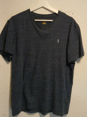 Mörkblå t-shirt från Ralph Lauren - Snygg mörkblå t-shirt från Ralph Lauren med klassisk v-ringning och broderad logga på bröstet. T-shirten har en avslappnad passform och är tillverkad i mjuk bomull, perfekt för en stilren vardagslook.