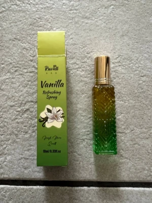 Vanilla Refreshing Spray 10ml - Fräsch parfym med vaniljdoft i en snygg glasflaska med guldfärgat lock. Flaskan har ett mönstrat glas i gröna och gula toner. Kommer i en grön förpackning med blommotiv och texten 'Vanilla Refreshing Spray'. Perfekt storlek för väskan.
