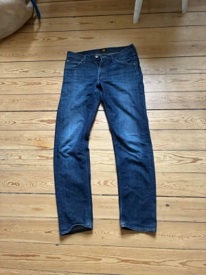 Mörkblå jeans från Lee - Snygga mörkblå jeans från Lee med klassisk femficksdesign och raka ben. Jeansen har en tydlig Lee-logga på bakfickan och är tillverkade i denim. Perfekta för en avslappnad och trendig look.