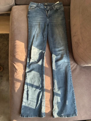 Blå bootcut jeans från ONLY - Säljer ett par blå bootcut jeans från ONLY Blue Denim. Jeansen har klassisk femficksmodell, normalhög midja och lätt slitningar framtill för en avslappnad look. Tillverkade i mjukt denimtyg som sitter skönt hela dagen.