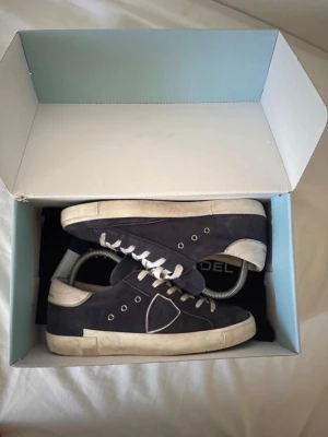 Philippe Model mörkblå sneakers - Mörkblå sneakers från Philippe Model i mocka med vita detaljer och vit sula. Klassisk låg modell med vita skosnören  diskret logga på sidan. Perfekta för en stilren och avslappnad 