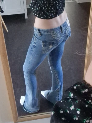 True Religion joey w24 - Säljer ett par blå bootcut jeans från True Religion med detaljerade broderier. Välsigt bra skick utöver slitningar på hälarna(se bild), slitningarna syns dock inte när jeansen sitter på, nypris 1599! Storlek w24 jag skulle säga att de är en xs/s och är väldigt stretchiga. Skriv om fler frågor🙌