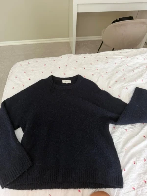 Mörkblå stickad tröja Gina Tricot - Mysig mörkblå stickad tröja från Gina Tricot i ullblandning. Tröjan har rund halsringning, långa ärmar och ribbade muddar vid ärmslut och nederkant. Perfekt för kyliga dagar och enkel att matcha med jeans eller kjol.