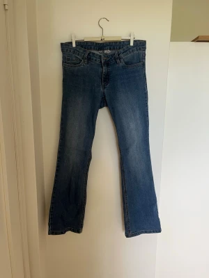 Blå bootcut jeans med medium midja - Säljer ett par klassiska blå bootcut jeans med medium midja och fickor. Jeansen har en lätt tvättad look och ben som går ut något nedtill. Perfekta för en avslappnad och trendig stil. Materialet är denim i bomull.