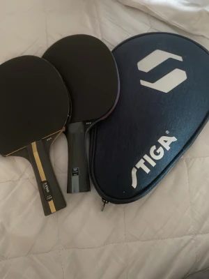 pingisracket med fodral - Två 3 stjärniga pingisracket  i svart med trähandtag och ett blått fodral med Stiga-logga. Perfekt för dig som vill spela bordtennis med kompisar. Racketarna har klassisk rund form och greppvänligt handtag.                                                 OPS!: kommer radera detta annons 10 juli eftersom att jag ska på semester”!