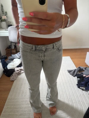 Ljusgrå lågmidjade bootcut jeans - Säljer ett par ljusgrå jeans med rak passform och klassisk femficksdesign. Jeansen har låg midja och är tillverkade i ett mjukt denimtyg som ger en avslappnad look. Perfekta till en enkel topp eller hoodie.