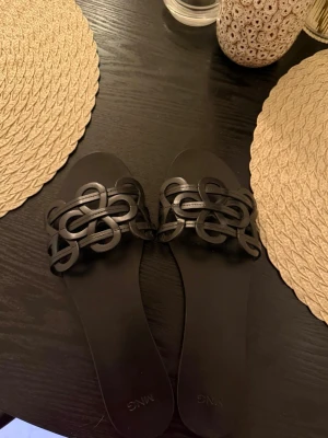 Svarta flätade sandaler från Mango - Säljer ett par stilrena svarta sandaler från Mango med flätad remdesign över foten. Sandalerna har öppen tå och platt sula, perfekta för sommardagar. Använda en gång i någon timme, skicket är så gott som nytt. Storlek 40 men passar som 39.