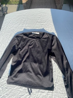 Ribbad långärmad topp med knytning bak - Säljer en snygg svart långärmad croppad topp med öppen rygg och knytning baktill. Tröjan är ribbad och är från NA-KD i storlek M. Perfekt fest topp🤩☺️