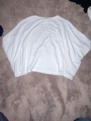 Vit oversized tröja från Nelly - Säljer en vit oversized tröja från Nelly med avslappnad passform och rund halsringning. Tröjan har breda ärmar och är gjord i ett mjukt, stretchigt material som känns skönt mot huden. Perfekt för en chill och enkel look. En lite fläck vid axeln.