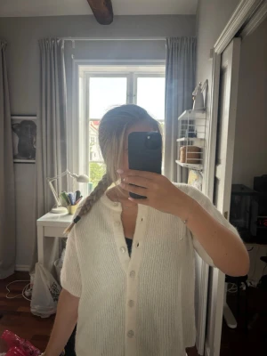 Vit kortärmad kofta med knappar - Mysig vit kofta med korta ärmar och rund hals. Koftan har en rak passform och stängs med knappar framtill. Perfekt att slänga över ett linne eller t-shirt för en enkel och clean look.
