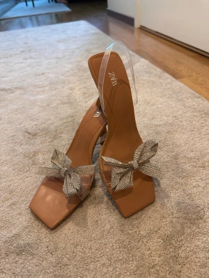 Beige pumps med strassrosett från Zara - Snygga beige pumps från Zara.Har använt den en gång.