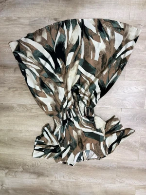 Mönstrad kortklänning med volang - Snygg kortklänning med abstrakt mönster i brunt, beige, svart och vitt. Klänningen har volangdetaljer vid ärmarna och markerad midja med resår. Perfekt för dig som gillar unika prints och bekväm passform.
